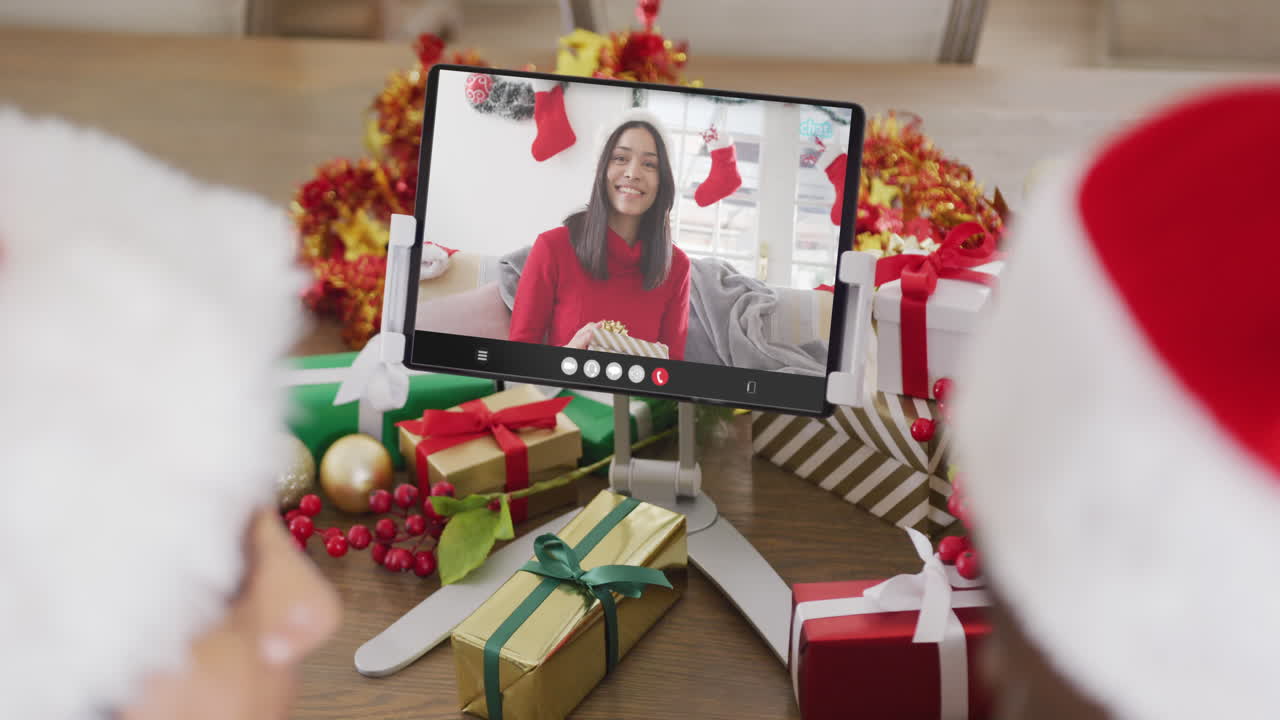una pareja diversa con sombreros de santa haciendo una llamada de video con una mujer biracial.
