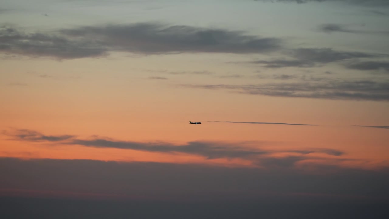 Silhuet af passagerfly flyver gennem levende orange og blå gradienthimmel ved solnedgang med spredte skyer.