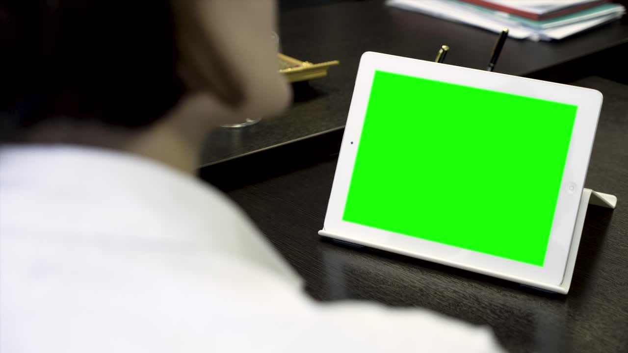 사무실의 책상 위에 초록색 화면을 가진 색 태블릿을 사용하는 사람.