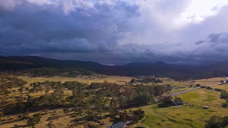 aerial cinematográfica de nubes de lluvia oscuras sobre el parque nacional de kosciuszko con tierras de cultivo doradas en primer plano, crackenback, nsw, australia