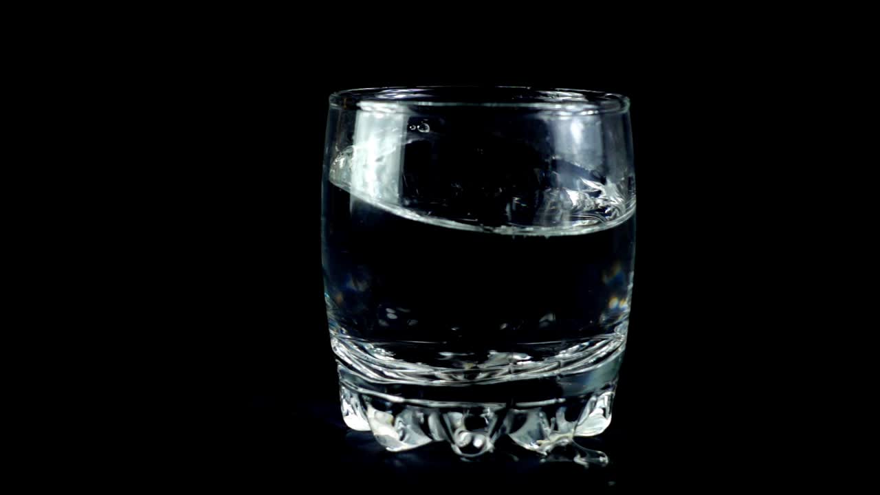 Vand i et glas på en sort baggrund. Slowmotion.