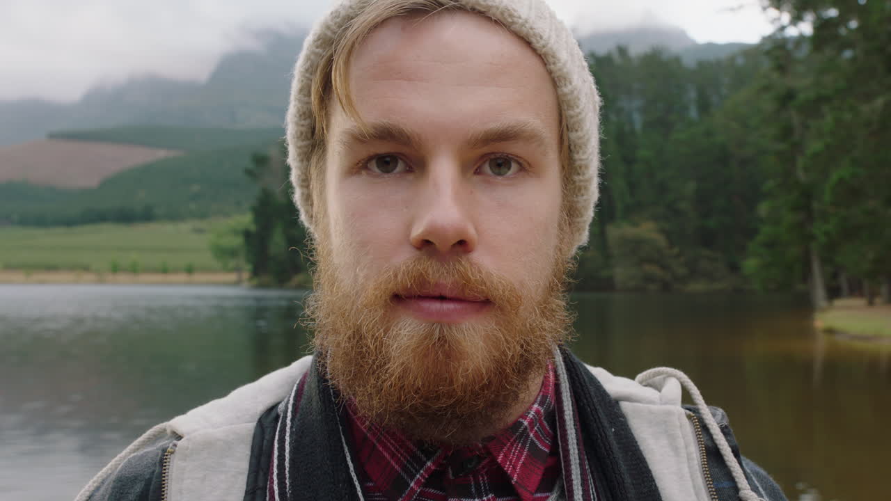 портрет рыжеволосый хипстер мужчина с бородой серьезный взгляд на природе у озера в шапке-бини 4k