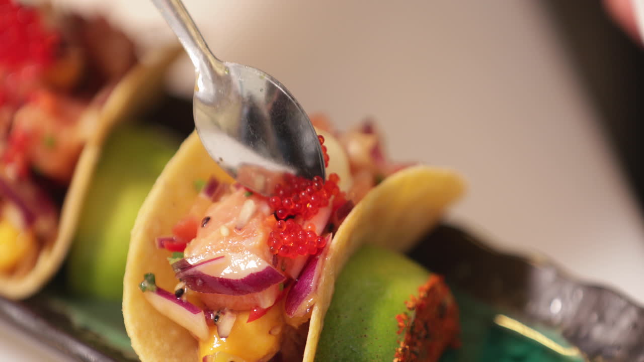 Cuoco in cucina che sistema caviale rosso su taco di sushi usando un cucchiaino