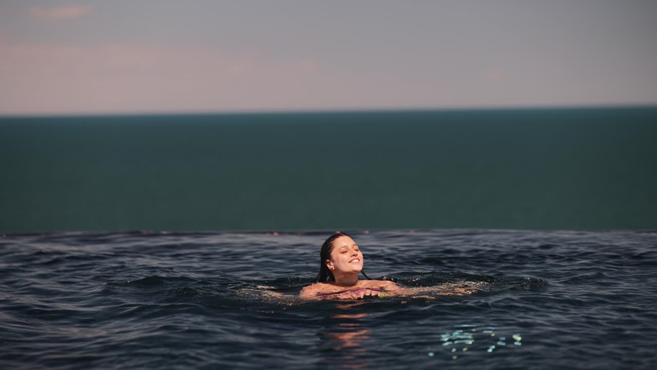 바다를 볼 수 있는 무한 수영장에서 수영하는 여자