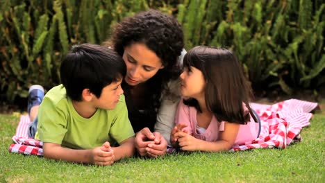 Mujer-Joven-Tumbada-En-El-Césped-Charlando-Con-Sus-Hijos.