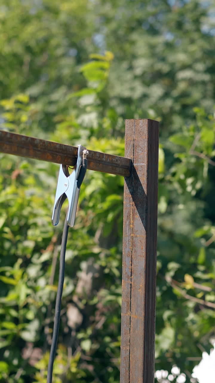 vista posteriore di un costruttore con maschera da saldatore che applica un morsetto sulla parte superiore della carcassa di una recinzione metallica arrugginita in giardino