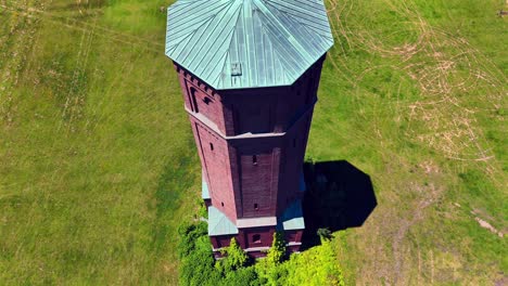 An-aerial-view-of-a-tall-brick-water-tower-on-a-sunny-day-in-a-large-green-field-on-the-Pilgrim-Psychiatric-Center-on-Long-Island,-NY