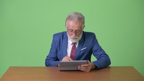 handsome senior bearded businessman against green background
