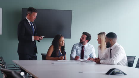 group collaborating on task at graduate recruitment assessment day whilst being observed by mature businessman