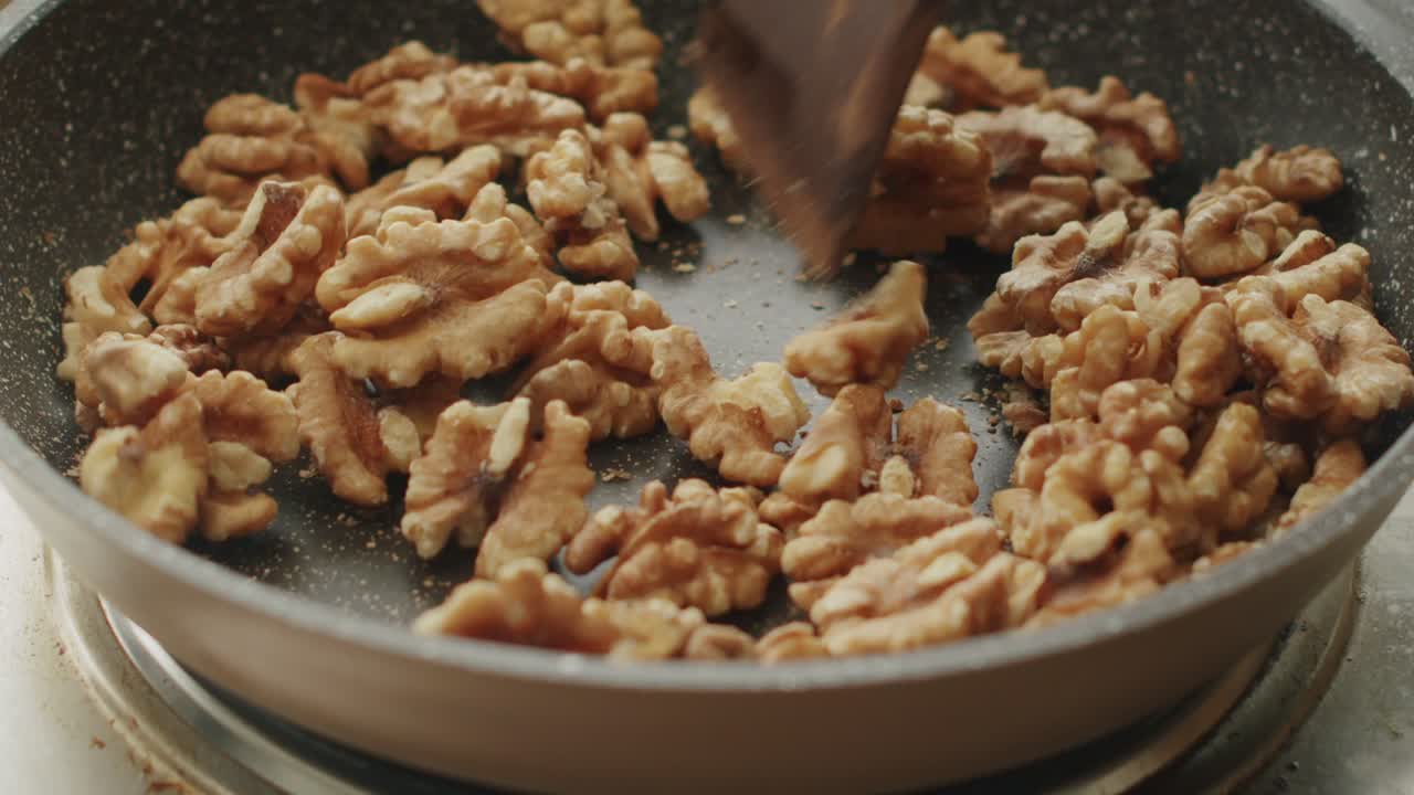 Anonymous person frying walnuts in pan in kitchen