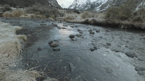 Toma-Panorámica-De-Un-Río-Que-Corre-Rodeado-De-Montañas-Nevadas-En-Nueva-Zelanda-Durante-El-Invierno