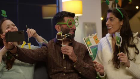 group of friends dressing up at home or in bar celebrating at st patrick's day party posing for selfie on phone 2