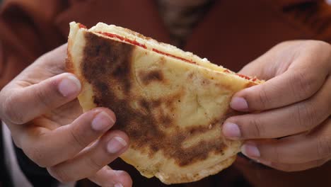 close-up of a person holding a delicious sandwich with cheese, tomato sauce, and egg