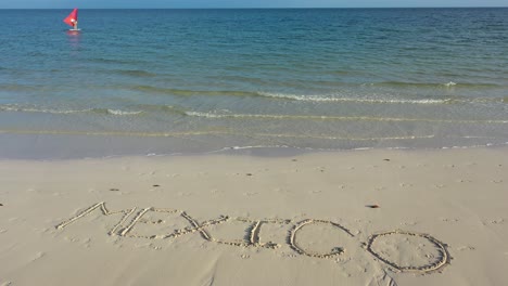 turning shot of mexico inscribed in the sand on a beach with windsurfer in the distance