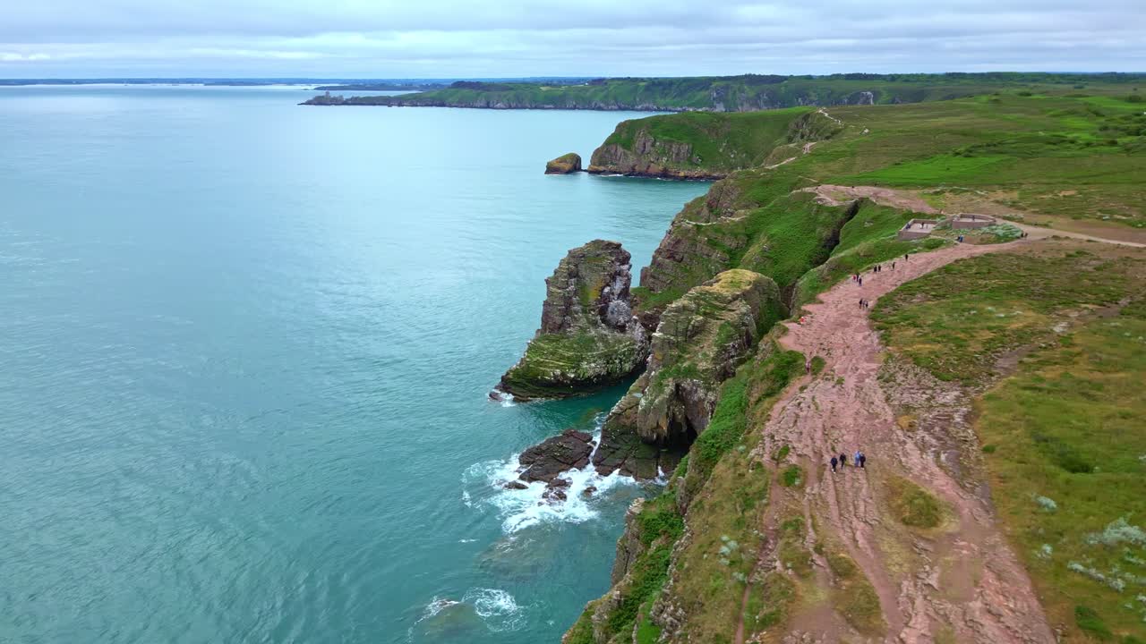 Side drone view of Cap Fréhel cliffs, crashing waves, rocky coast, and ocean horizon.