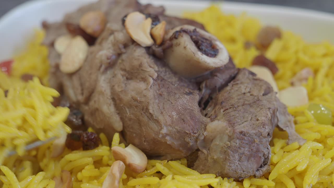 cerca de un plato de arroz amarillo con cordero, almendras y pasas