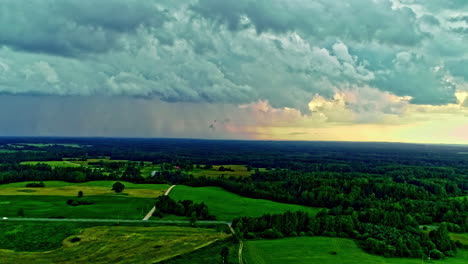 stormy heavy clouds are floating above lush green fields and forests in rural latvia