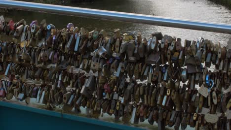 Multiple-padlocks-connected-to-railings-on-bridge-over-water