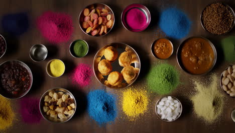 colorful holi powders and various indian dishes on a wooden table