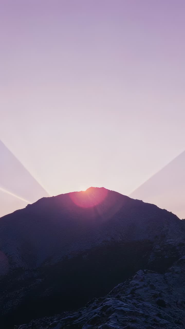 Vertical video: Peeking sun and mountain ridge casting rays at dawn, lens flare, shadowed slopes
