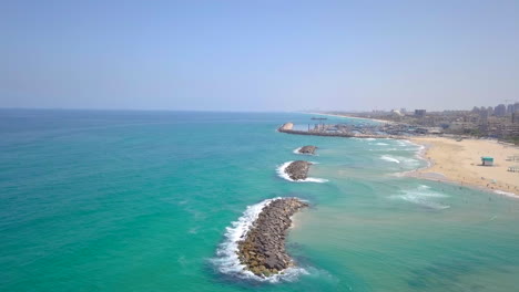 sunny summer aerial in israel, ashkelon beach - pan from the ocean over rock dams to the city