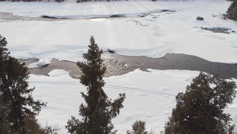 Paralleler-Drohnenflug-Aus-Der-Luft-Stromaufwärts-Einer-Friedlichen-Winterlandschaft-Und-Eines-Flusses