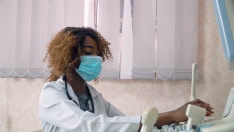 african american woman doctor in protective mask examines patient in ultrasound device monitor. coronavirus diagnosis