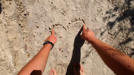 pov shot of man drawing a heart on the sand