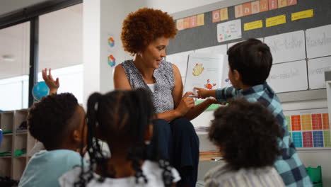 Eine-Lehrerin-Liest-Multikulturellen-Grundschülern-Im-Unterricht-Vor-Und-Stellt-Ihnen-Fragen