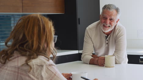 Senior-Hispanic-Couple-Talking-And-Drinking-Coffee-As-They-Relax-In-Kitchen-At-Home-Together