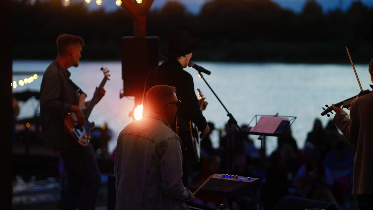 夕焼けの湖畔ステージで音楽を演奏するライブバンド