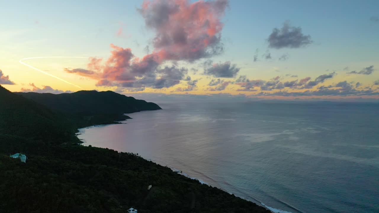 Dramatic aerial view features St. Croix’s island point silhouetted against a vibrant, colorful sky while calm ocean waters sparkle gently under the glowing horizon