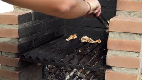 close up of person turning chicken pieces being prepared on grill