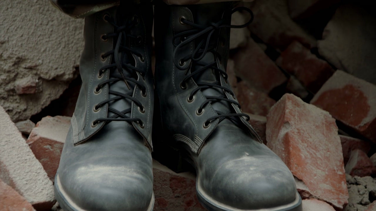 Worn Military Boots On Rubble Closeup Shows Camoclad Soldier Standing Among Broken Bricks And Concrete,