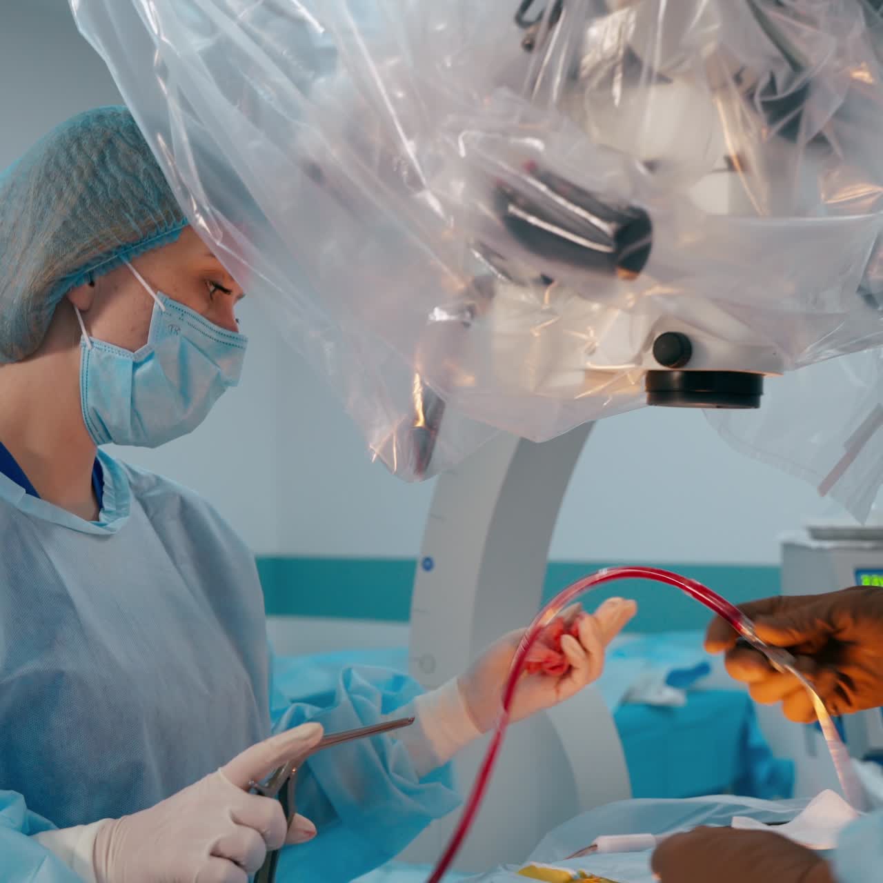 Operating process in clinic. Female assistant giving medical instruments to the surgeon. Doctor uses contemporary microscope during the surgery.