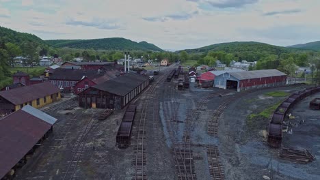 Una-Vista-Aérea-De-Una-Carretera-Ferroviaria-De-Carbón-De-Vía-Estrecha-Abandonada-Con-Tolvas-Oxidadas-Y-Vagones-De-Carga-Y-Un-Edificio-De-Apoyo-Que-Comienza-A-Restaurarse