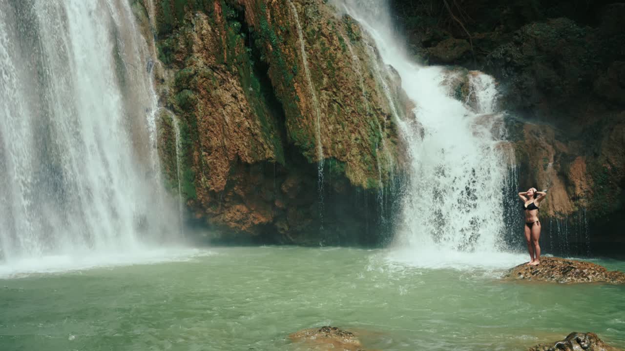Shot of a woman standing on a rock beneath the falls, gazing upward, evoking freedom and connection to nature.