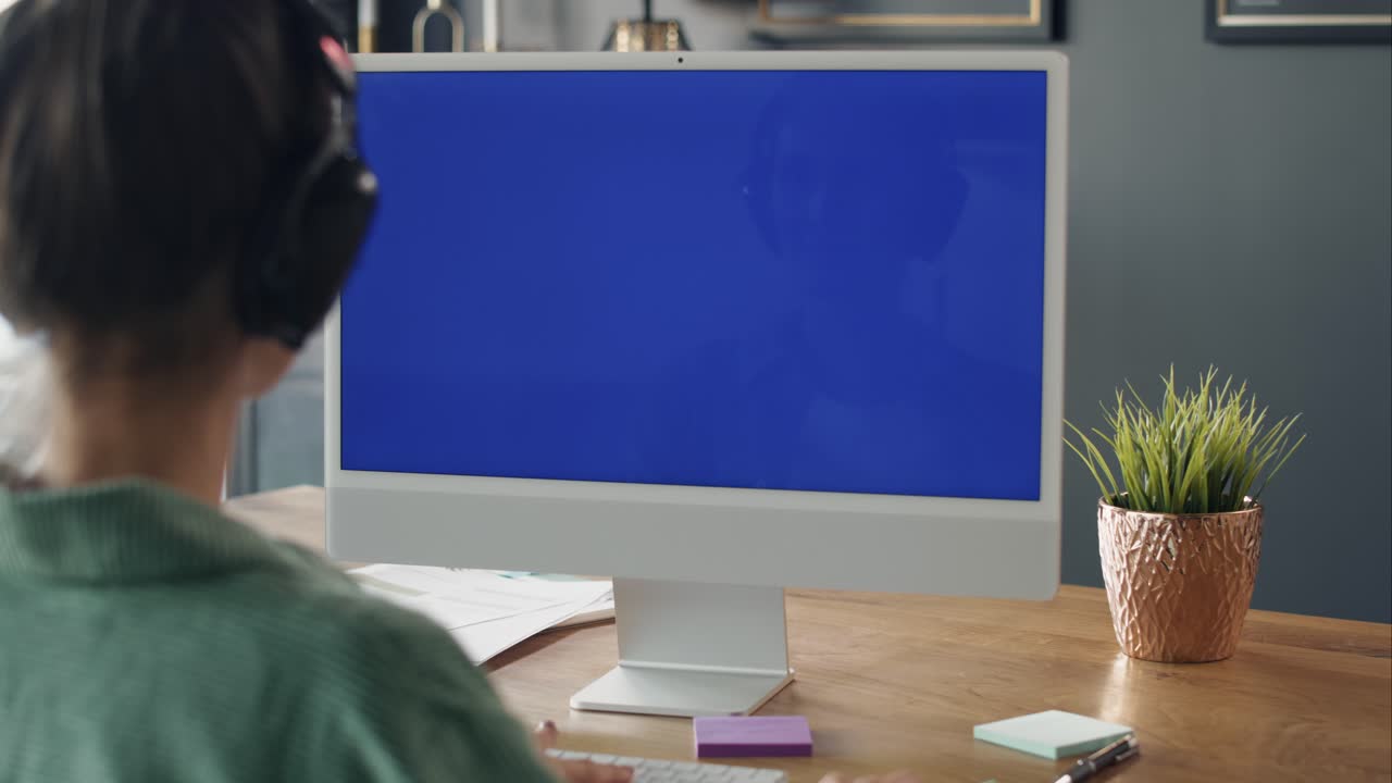 vista trasera de una mujer trabajando en una computadora con pantalla azul.