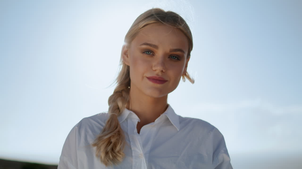 Rolig pige poserer i naturen, vertikalt portræt. Blond, glad kvinde varmer sig i solens stråler.