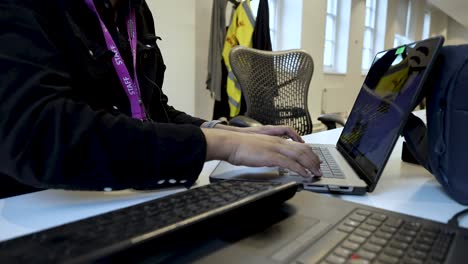 An-individual-is-using-a-laptop-within-an-indoor-office-setting,-illustrating-the-notion-of-digital-labor-and-managing-tasks