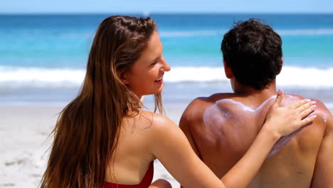 una mujer aplicando protector solar a su novio.