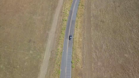 4K-drone-shot-moving-forward-down-country-road-tilt-up-slowly-to-reveal-beautiful-landscape-and-long-road-winding-through-California-rural-fields,-stretching-out-as-far-as-eye-can-see