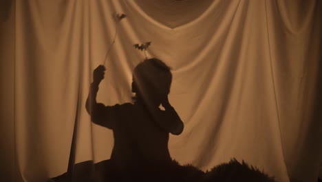 silhouette of little boy telling spooky stories using shadow play and paper bats - silhouette of little boy telling spooky stories using shadow play and paper bats. child of primary age spend leisure, sitting behind curtain at home. puppet theater of shadows. performance for family, holiday, hallowe