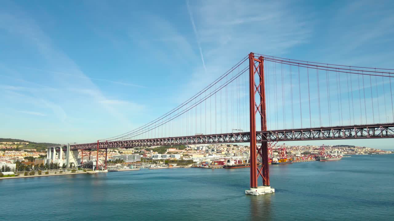 Video aereo realizzato con drone che sorvola l'ampio fiume Tago a Lisbona, di colore rosso, in una giornata di sole, con auto, veicoli e treni in movimento. Lisbona, città del Portogallo, sullo sfondo