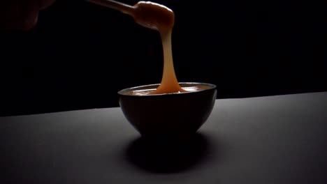 disparo en cámara lenta de una mano agarrando un dipper de un cuenco con miel contra un fondo negro
