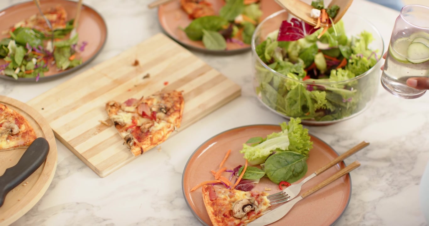Posate da insalata in legno che iniziano a mescolare l'insalata in una ciotola di vetro trasparente su un tavolo di marmo, piatti da portata