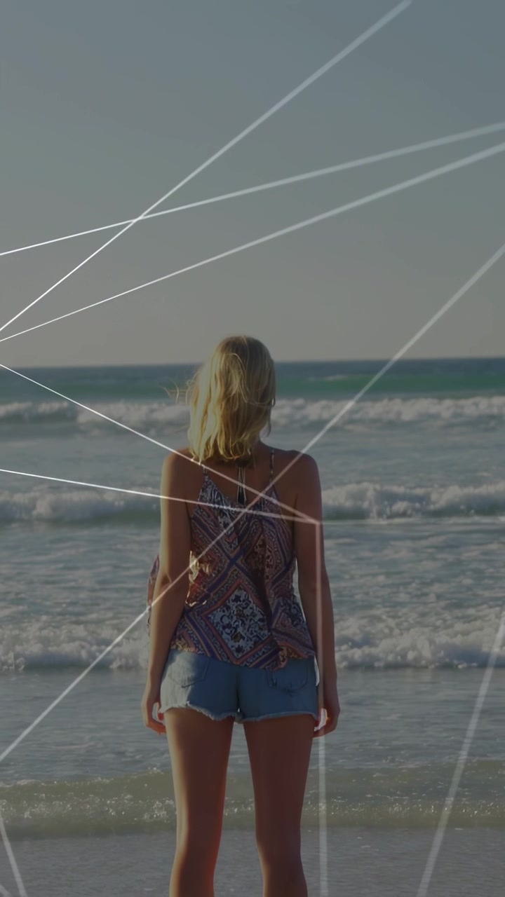 Vertical video: Pullback showing woman walking into sea, watching sea, tech lines crossing her