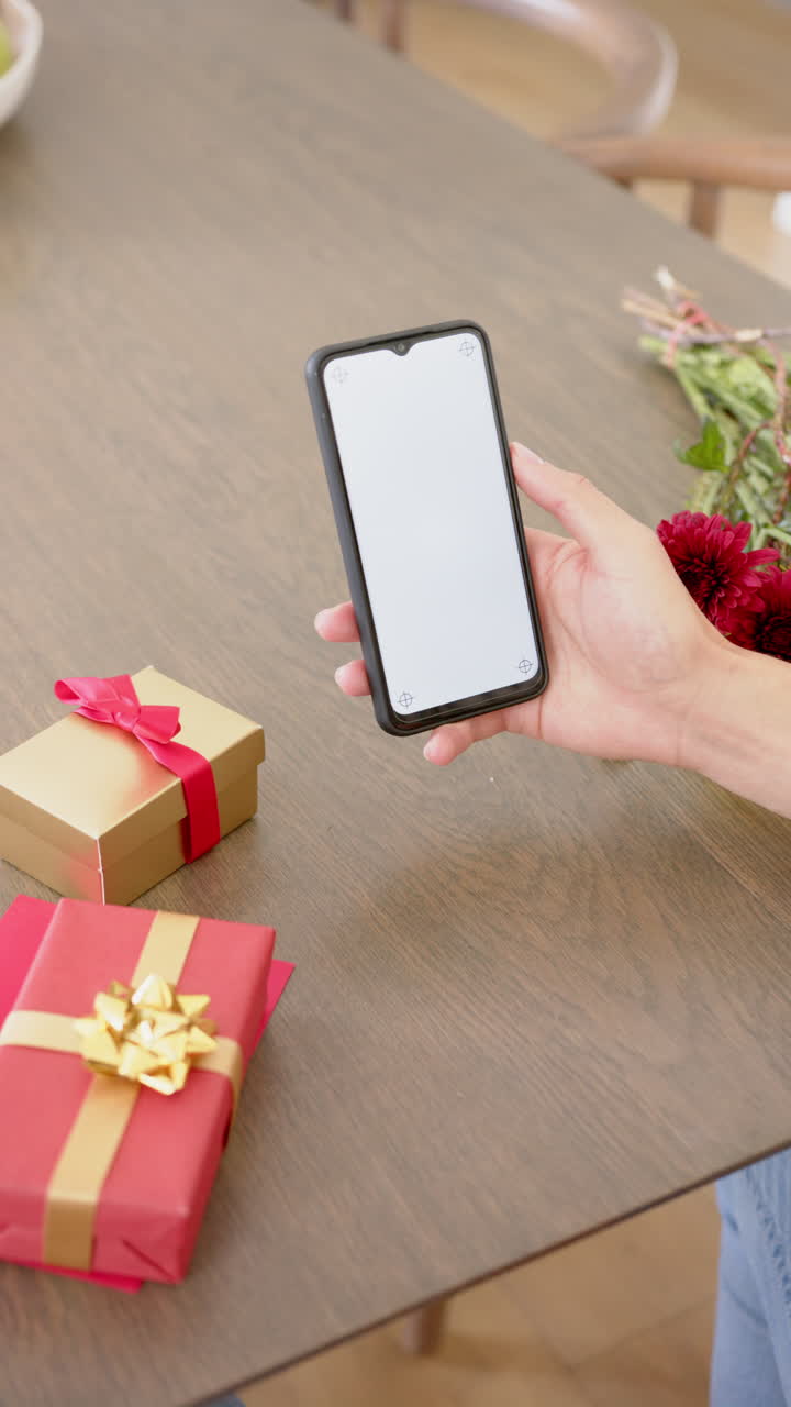 Vertical video of biracial man with gifts having smartphone video call with copy space, slow motion