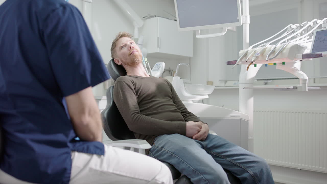 Dentist speaking to male dental patient sitting in reclined chair of clinic