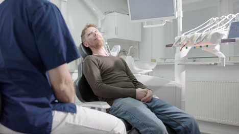 dentist speaking to male dental patient sitting in reclined chair of clinic